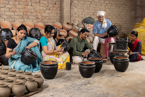 Happy Indian family of potters painting and polishing pot together at workshop