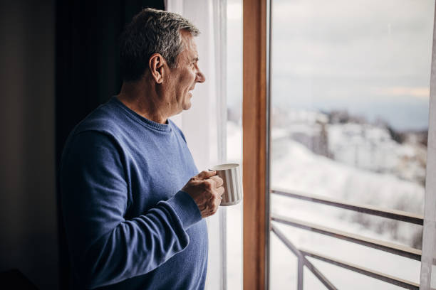The man is drinking coffee looking out the window