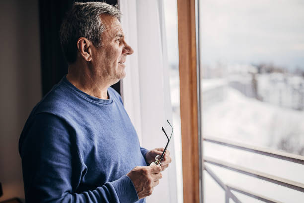 istock An older man is standing by the window 1362715625