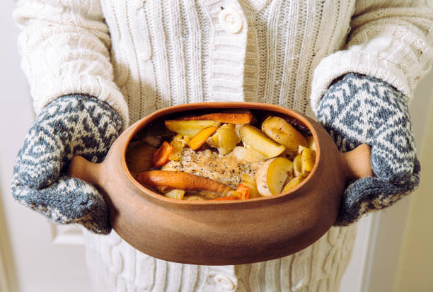 Woman holding terracotta clay cooking pot with slow cooked pork roast and vegetables inside. Wearing knitted clothing, winter comfort food concept. Woman holding terracotta clay cooking pot with slow cooked pork roast and vegetables inside. Wearing knitted clothing, winter comfort food concept. comfort food stock pictures, royalty-free photos & images