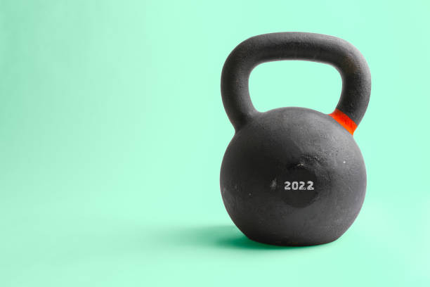 Horizontal studio shot of heavy black kettlebell with number 2022 on it, isolated on green background. Concept for new year resolutions, difficult year 2022 ahead. stock photo