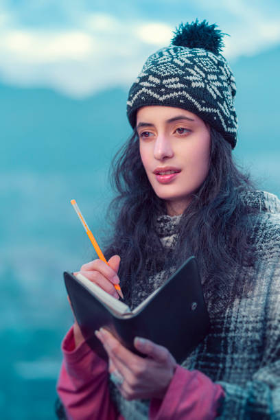 Young woman writes in a diary standing in hills. stock photo