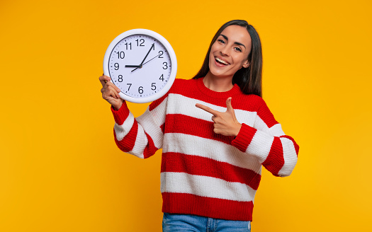 Time for study! Close up photo of happy modern student woman while she pointing on big white clock in her hands