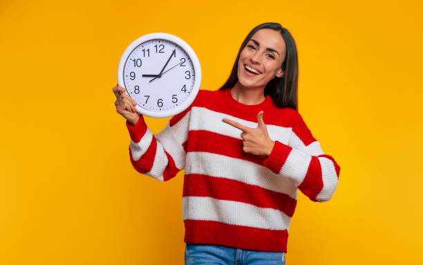 Time for study! Close up photo of happy modern student woman while she pointing on big white clock in her hands stock photo
