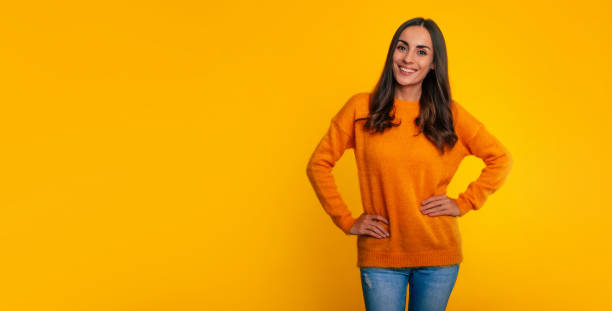 Close up portrait of happy beautiful modern confident brunette woman in yellow sweater while she posing with smile on yellow background stock photo