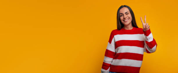 istock Charming smiling young modern woman shows victory sign while she posing isolated on yellow wall 1362724548