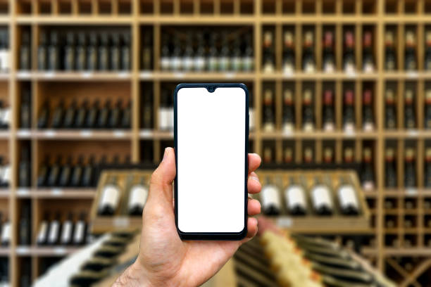 wine shop with bottles background. hand with blank smartphone screen one wine backdrop. buying and ordering alcoholic beverages online - wine bottle wine residential structure alcohol imagens e fotografias de stock