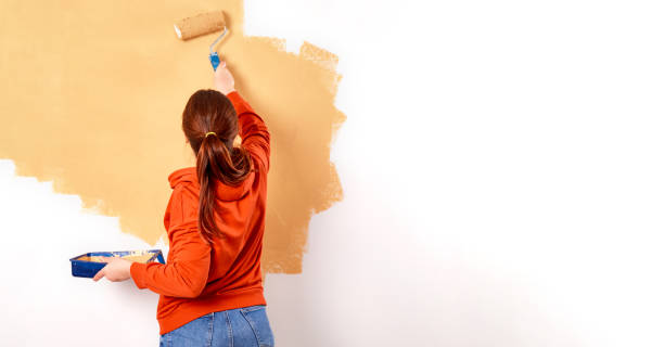 smiling caucasian woman painting interior wall of home. renovation apartment. repair and redecoration concept. copy space - pintar parede imagens e fotografias de stock