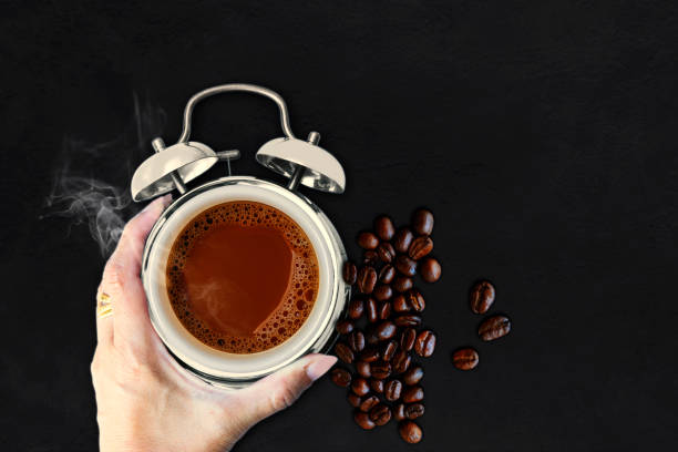 Hand holding coffee alarm clock cup and smoke on black stone background with copy space - Close-up coffee beans. Macro coffee beans and smoke in a alarm clock cup stock photo