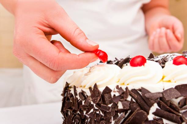 Hands of a female confectioner decorating a Black Forest gateaux with candied cherries. This image is part of a series in which a Black Forest cake is being prepared step by step.