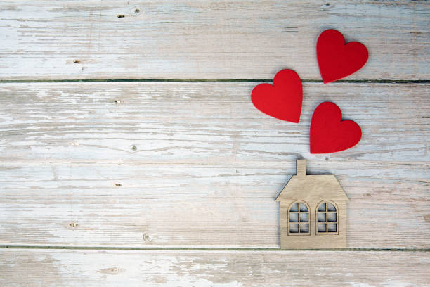 Wooden house with three red hearts on a wooden background. Love nest, love relationships. Buying a house with a young family. Affordable housing. banner. Family psychology, strong relations. copy space top view background stock photo