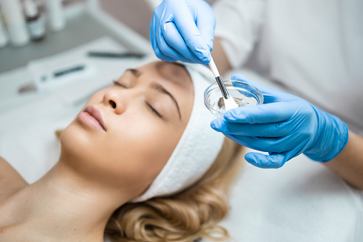 Doctor cosmetologist applies a transparent moisturizing mask to a woman's face. Face skin preparation for the ultrasonic peeling procedure