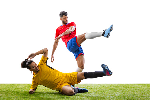 Leg kick. Soccer or football players in motion on grass flooring isolated on white background. Sportsmen wearing football kit jumping and running. Concept of motion and action, sport, lifestyle.