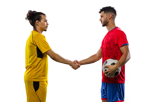 Young soccer or football players greeting each other on grass flooring isolated on white background. Sportsmen wearing football kits. Concept of motion and action, sport, healthy lifestyle.