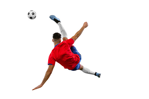 Young soccer soccer player looks confident practicing kicking ball in motion against white background on green grass. Football school. Concept of game, sport, recreation, active lifestyle.