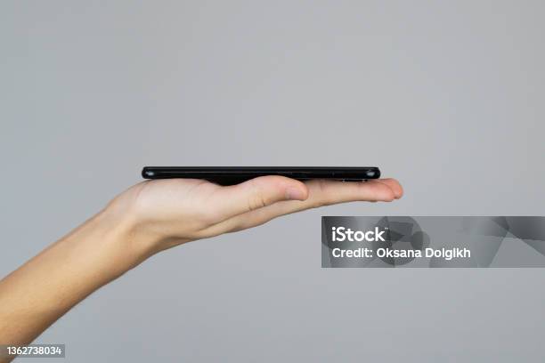 Hand Of A Teenager Holding Mobile Phone Side View For Presentation Studio Shot Template Or Mockup On A Grey Background Stock Photo - Download Image Now