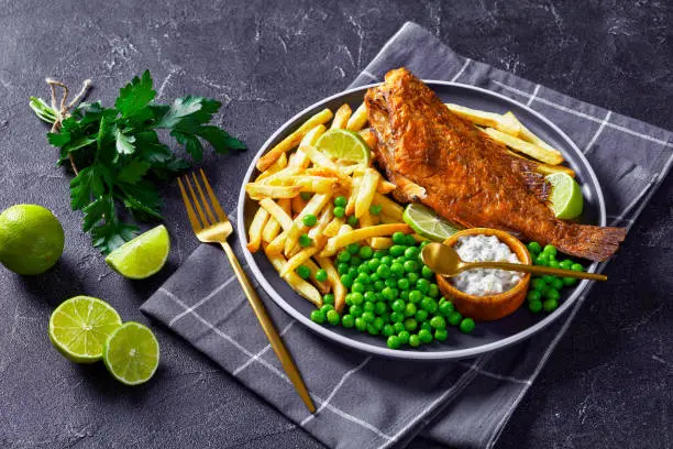 fried Atlantic redfish on a plate with potato chips, boiled green peas and lime slices, horizontal view from above, close-up
