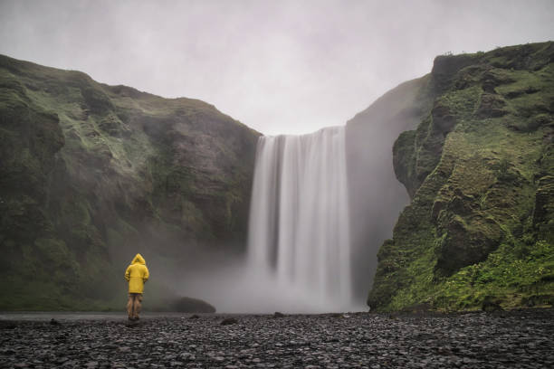man with yellow rain suit in front of skógafoss waterfall in iceland - hofmann imagens e fotografias de stock