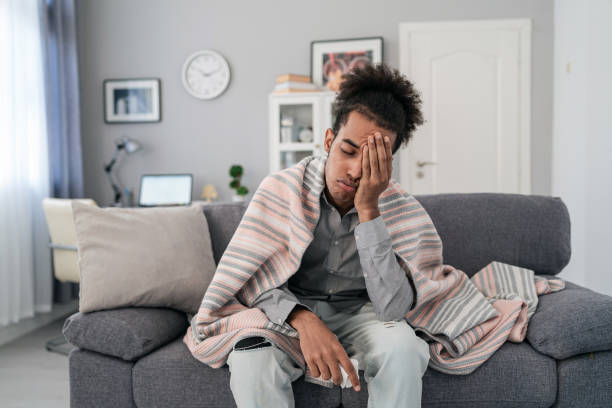 kuvapankkikuvat ja rojaltivapaat kuvat aiheesta nuori afroamerikkalainen mies, joka istuu sohvalla kotona, jolla on kuumetta ja päänsärkyä ja koskettaa otsaansa tarkistaakseen lämpötilansa - hangover