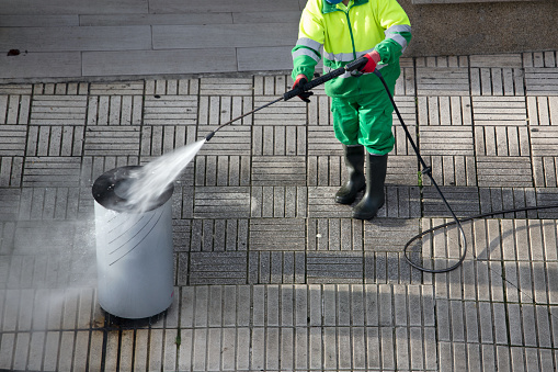 Sweeper cleaning a trash can on sidewalk with high pressure water jet machine. Street maintenance
