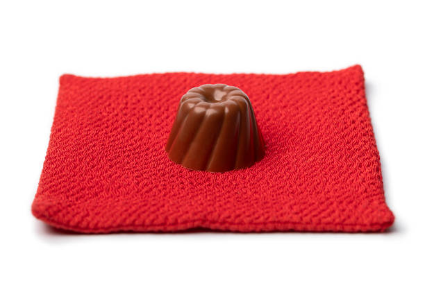 Single chocolate bonbon on a red pillow isolated on white background close up