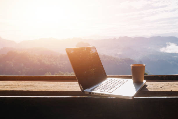 istock Computer Monitor, Keyboard, coffee cup and Mouse with Blank is on the work table at the sky mountain river and trees front view background. 1362752424