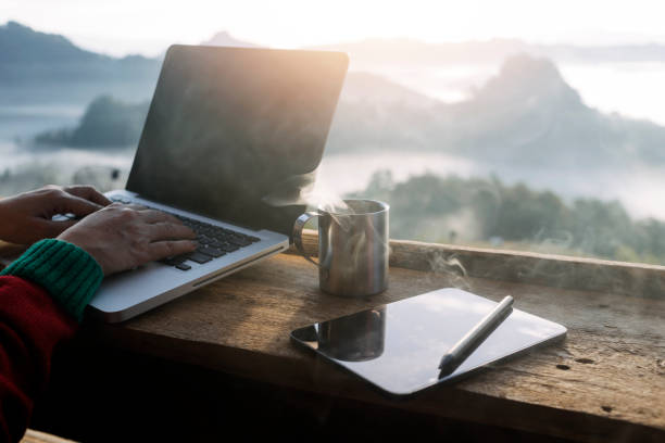 Computer Monitor, Keyboard, coffee cup and Mouse with Blank is on the work table at the sky mountain river and trees front view background.