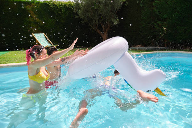 istock Two friends throwing man from a rainbow unicorn float into the pool. 1362754042