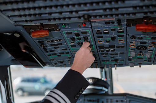 Close up of male airplane captain hand turning switch on cockpit overhead panel