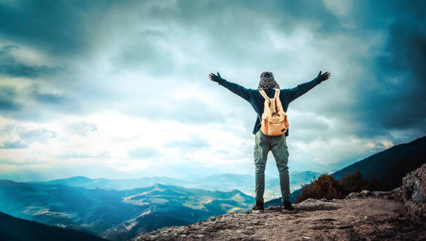 happy man with open arms standing on the top of mountain - hiker with backpack celebrating success outdoor - people, success and sport concept - on top of mountain peak success cold imagens e fotografias de stock