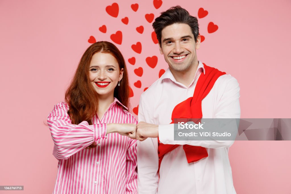Young smiling couple two friends woman man 20s in casual shirt look camera do fistbump gesture isolated on plain pastel pink background studio portrait. Valentine's Day birthday holiday party concept. Young smiling couple two friends woman man 20s in casual shirt look camera do fistbump gesture isolated on plain pastel pink background studio portrait. Valentine's Day birthday holiday party concept Smiling Stock Photo