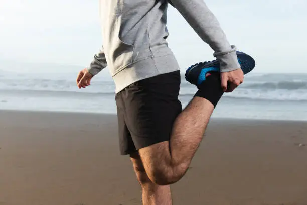 Closeup of quadriceps stretching. Warming up at the beach
