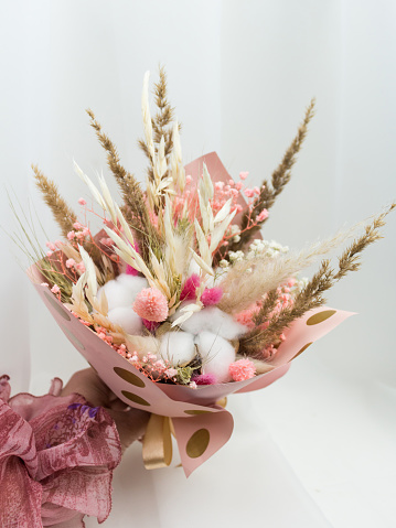 Bouquet pink, white, beige dried flowers in the hand on a white textile bsckground