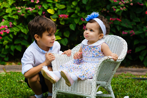 Beautiful one year old baby girl and older brother lifestyle portrait in a home garden setting.