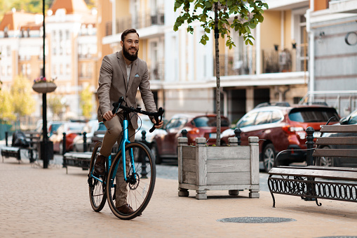 A businessman with a beard and in a suit rides a bicycle to work. Eco-friendly mode of transport, active lifestyle.