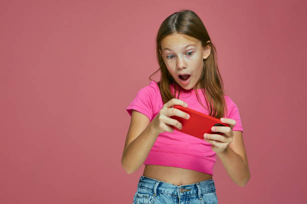 istock Amazed shocked child girl play game using mobile phone application on pink background. Children's addiction to gadgets 1362772578