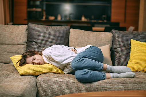Mujer joven poco saludable que sufre dolor menstrual, sostiene el vientre, tiene calambres abdominales durante el período acostado en el sofá photo