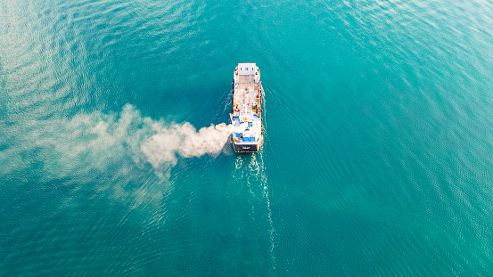 Aerial view of a container ship carrying cargo for an import-export logistics business in the ocean. Smoke from a ship sailing in the ocean - A picture from a drone of a ship carrying a cargo on the ocean. There is white smoke coming from the ship. Fishing vessel sailing on the sea. Sea photo. A boat sailing on the high seas.