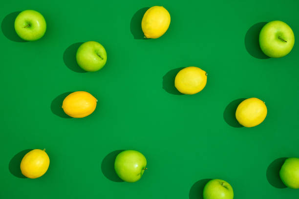 istock Trendy sunlight summer pattern made with yellow lemon and green apple on bright green background. Minimal summer concept. 1362778280