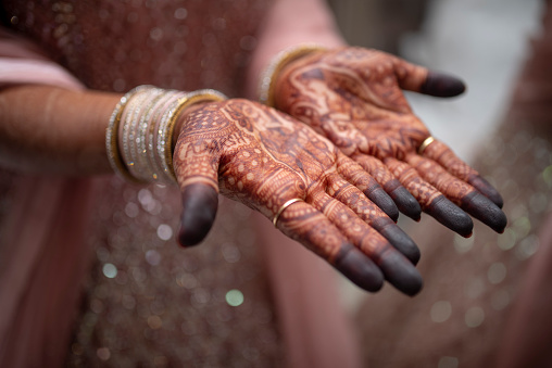 Traditional Indian woman hiding behind henna hand and she standing against black background.