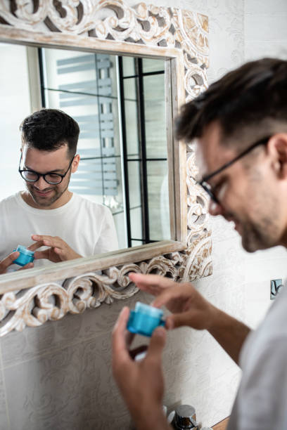 istock Young man going through morning routine in the bathroom applying face cream. 1362786455
