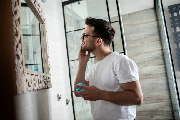 istock Young man going through morning routine in the bathroom applying face cream. 1362786686