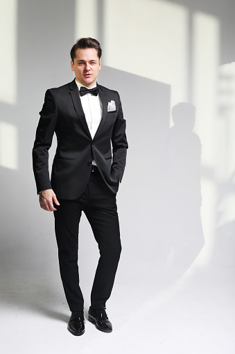 Young fashionable handsome man in a tuxedo and bow tie over white and grey background. Fashion concept.