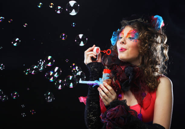 istock Fashionable young model female with creative make-up blowing soap bubbles. Doll style. Bright dress. Black background 1362794237