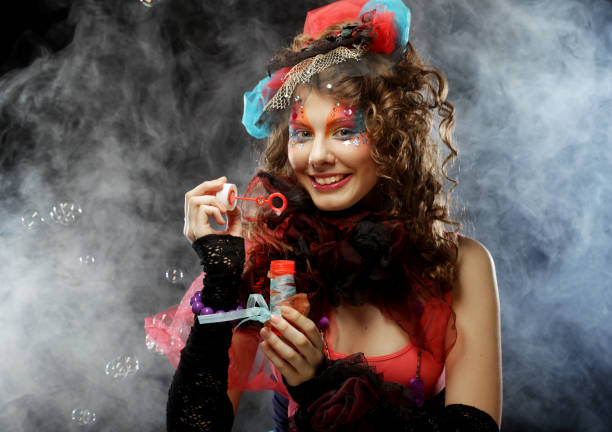 istock Fashionable young model female with creative make-up blowing soap bubbles. Doll style. Bright dress. Black background 1362794247