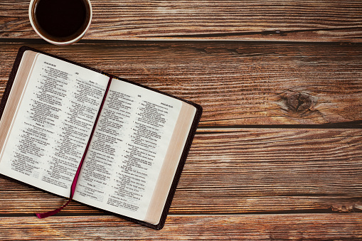 Open Holy Bible Book on wooden table background with a cup of coffee with copy space for text. The biblical concept of reading and studying the Scripture given by God Jesus Christ. Top view.