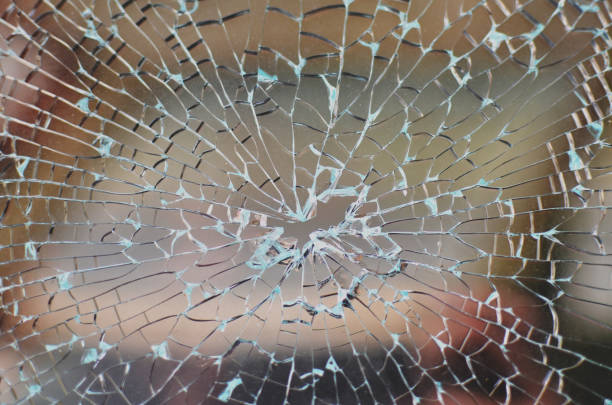 janela de carro quebrada com padrão de vidro rachado e um buraco de bala no meio - bullet hole hole glass destruction - fotografias e filmes do acervo