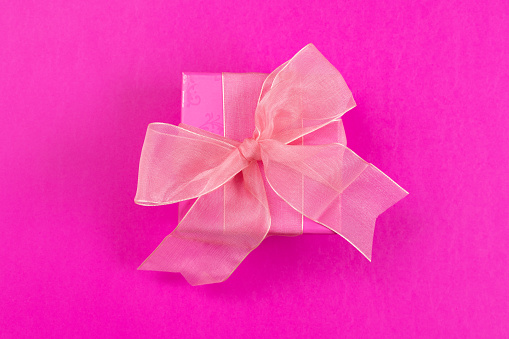 Pink gift box with pink bow on pink background. \nBox in the center. Monochromatic Simple Object Tabletop. Copy space.