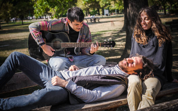 istock Friends play guitar and singing together while sitting on bench 1362810895