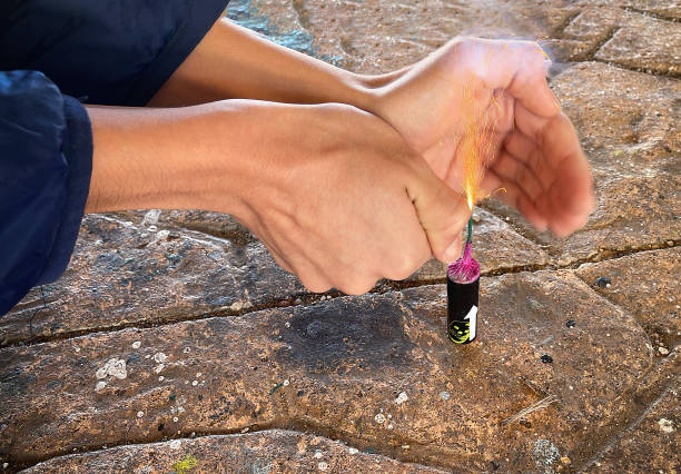 mains d’un enfant coquin avec un briquet allumant un gros pétard sur le sol, étincelles volant de la mèche de l’explosif sur le point d’exploser et d’exploser - firework explosive material photos et images de collection